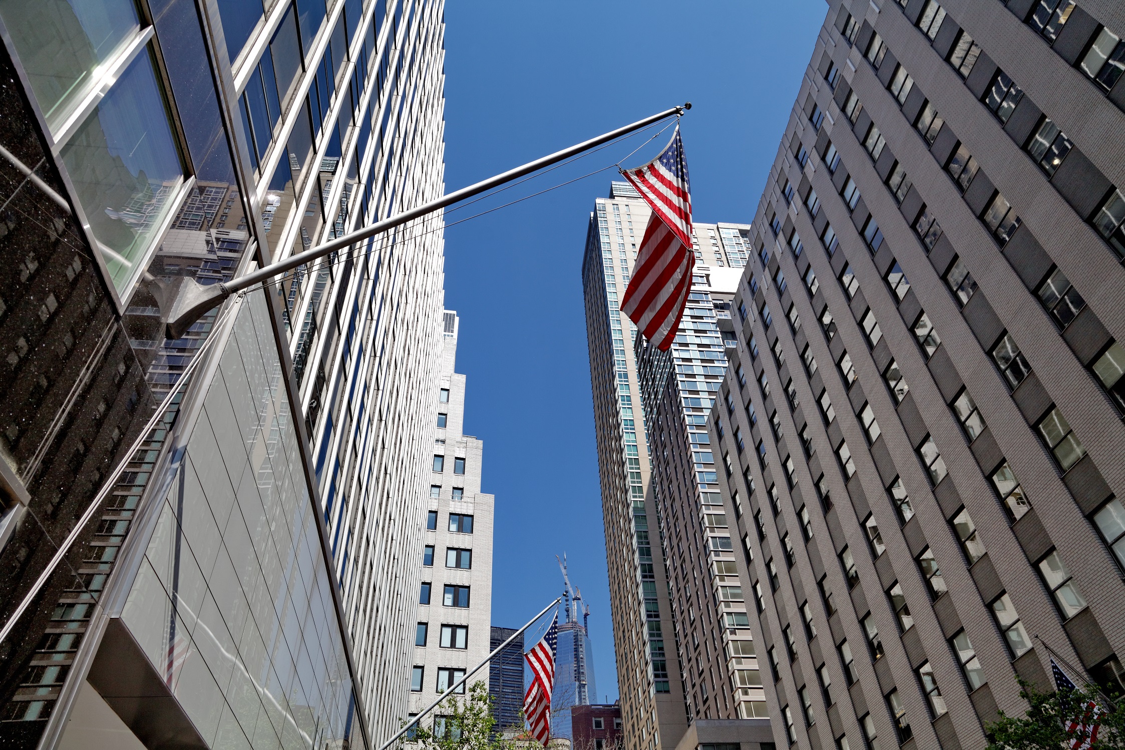 Blocks of Tall Office Buildings Pictured from Below Looking Up with Flagpoles with American Flags Protruding from Them